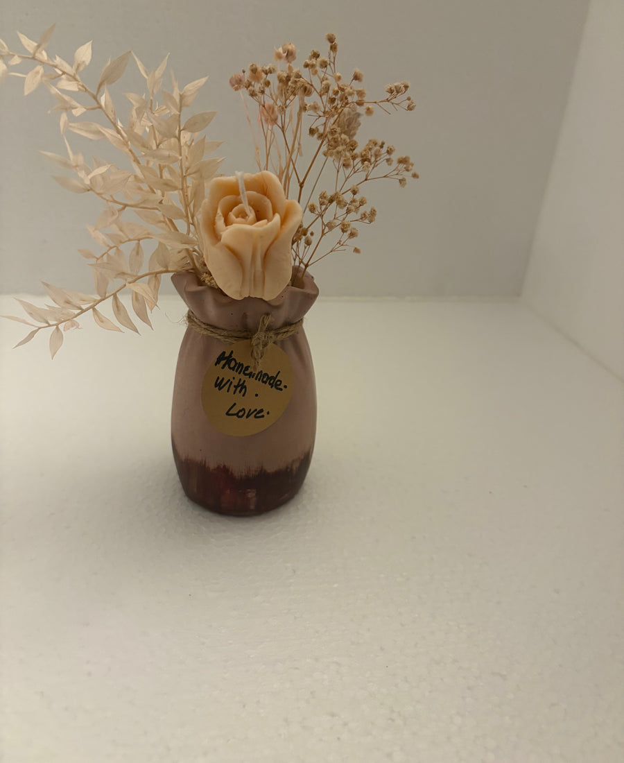 A small brown ceramic vase with a dark brown base, decorated with the words 'Handmade with Love' in black script. It is styled with dried flowers, including a prominent beige rose and baby's breath, set against a plain white background.